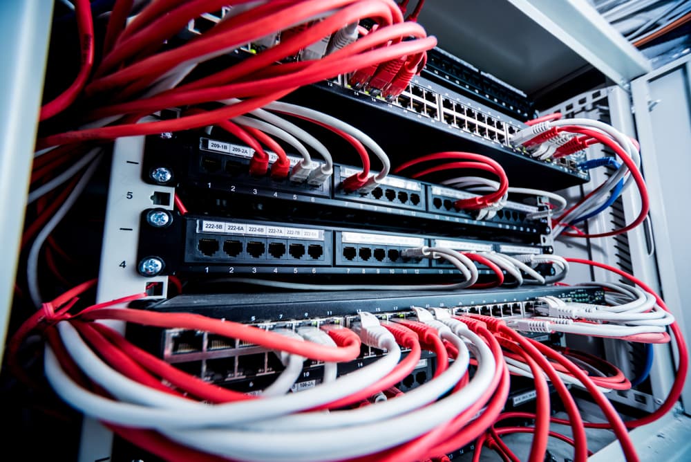 A network server rack with multiple switches and numerous red and white Ethernet cables connected, creating a complex web of connections.