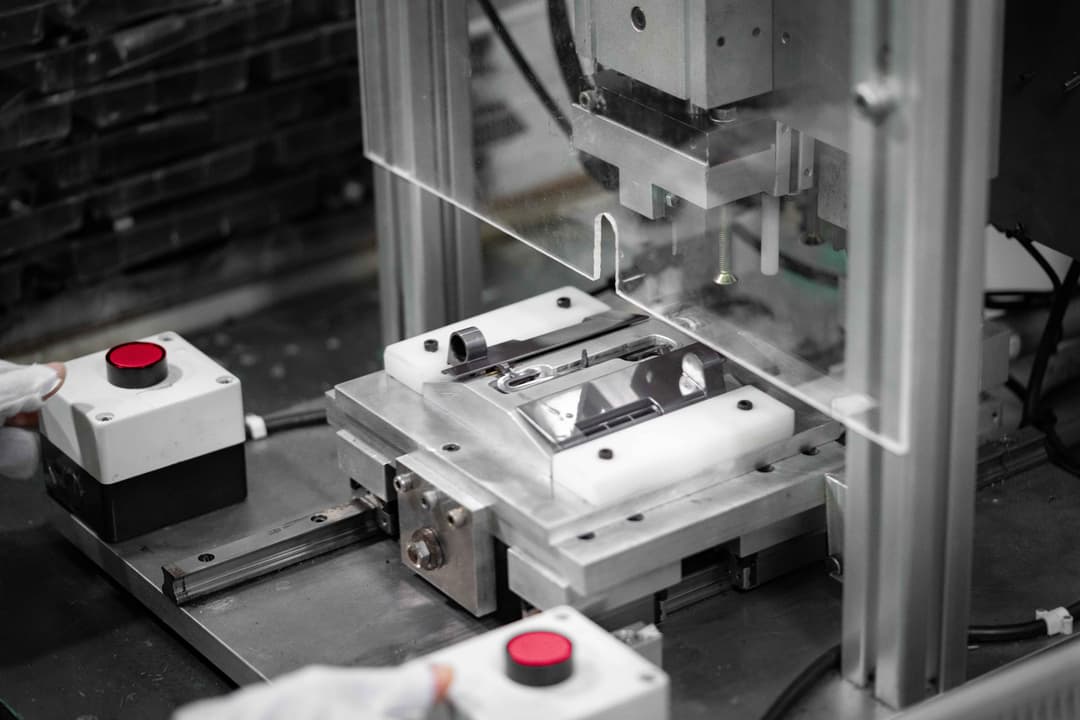 A gloved operator interacts with a manufacturing machine featuring exposed metal components and prominent red control buttons, emphasising hands-on operation and industrial precision.