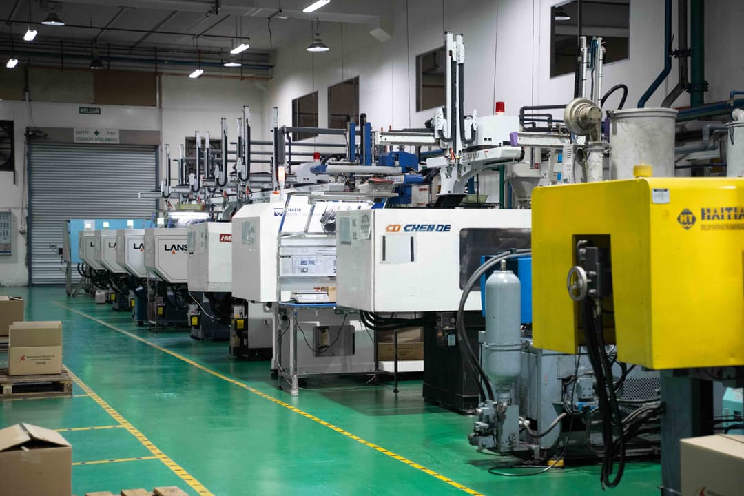 Several moulding machines lined up on a green factory floor under bright overhead lighting.